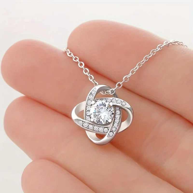 Love-knot pendant held between two fingers for scale